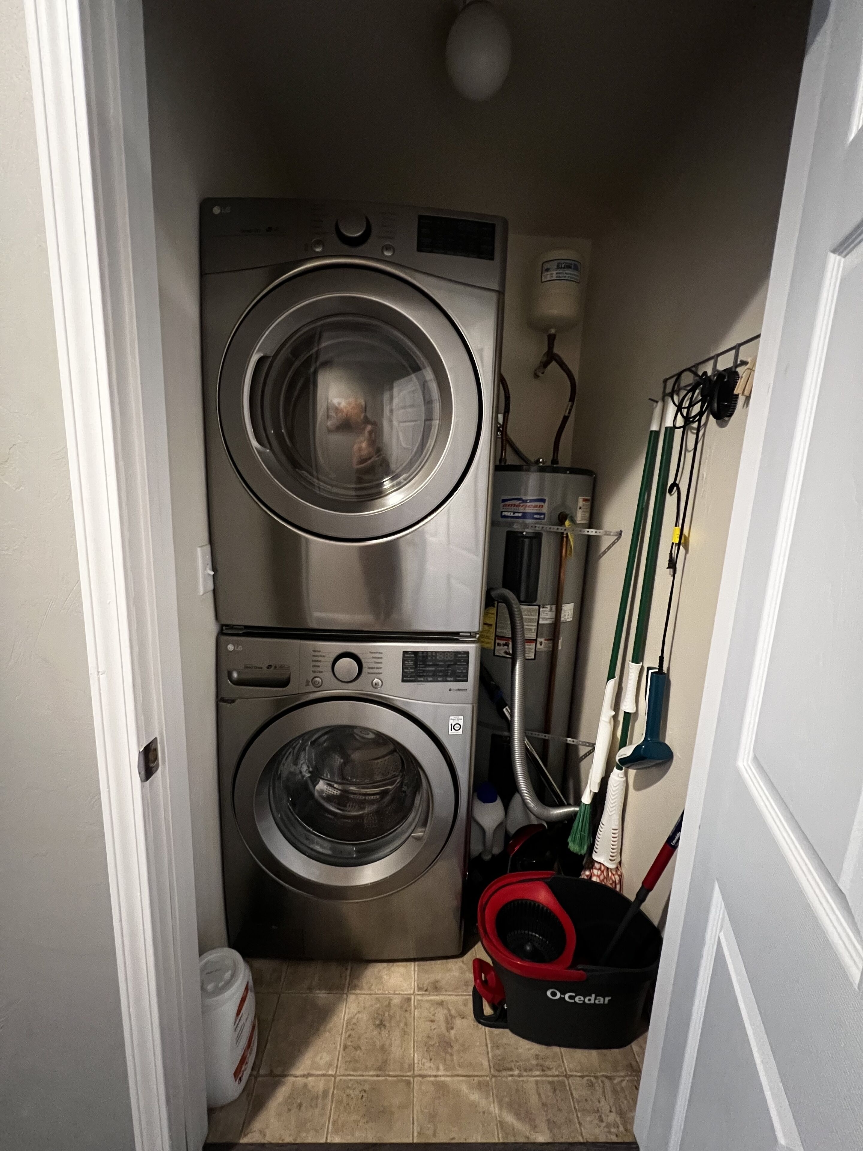 A laundry room with two stacked front-loading washing machines, a water heater, and cleaning supplies.