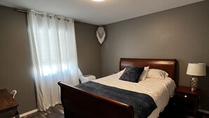 Een slaapkamer met een houten bed, een nachtkastje, een bureau, een stoel en een decoratieve wandversiering.