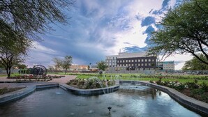 A public park with a fountain, surrounded by trees and buildings in the background. - Grand Aria Hotel (Gaborone)