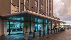 A hotel entrance with a covered walkway, glass doors, and potted plants. - Grand Aria Hotel (Gaborone)