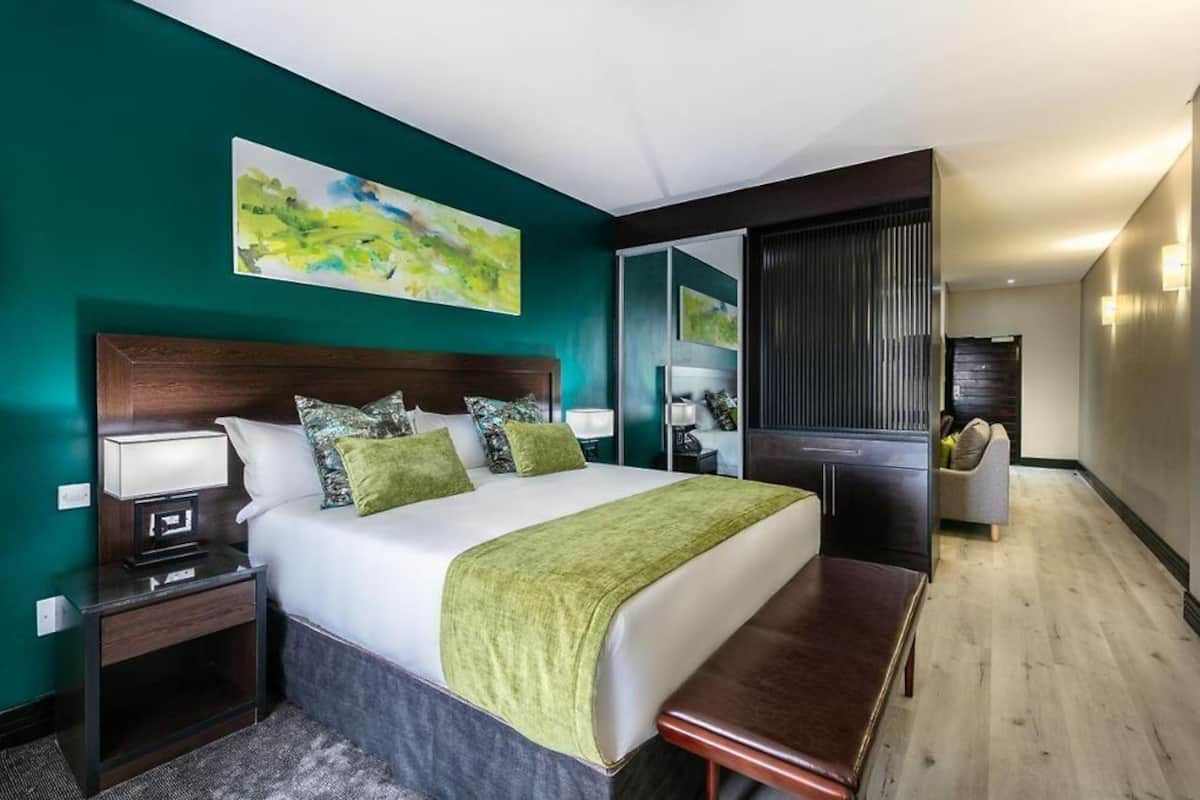 Quarto de hotel moderno com uma cama grande, um banco, uma mesa de cabeceira e um espelho.