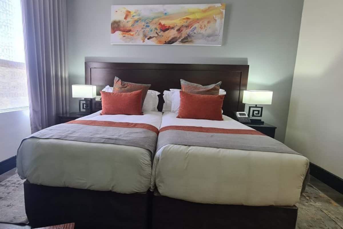 Uma cama de casal com duas almofadas, uma mesa de cabeceira com abajur e um quadro na parede.