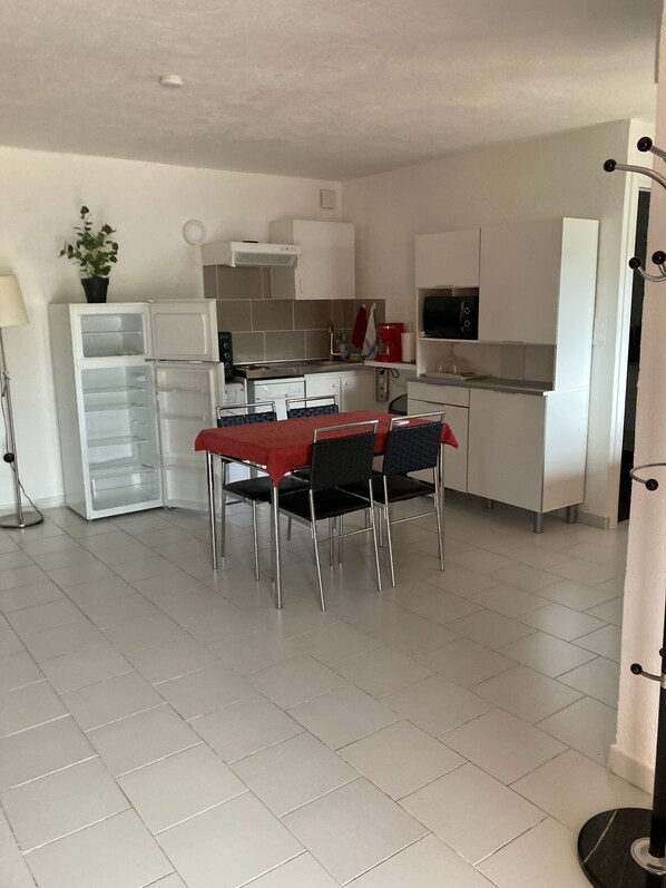 A modern kitchen with white cabinets, a dining table with four chairs, and a red tablecloth.