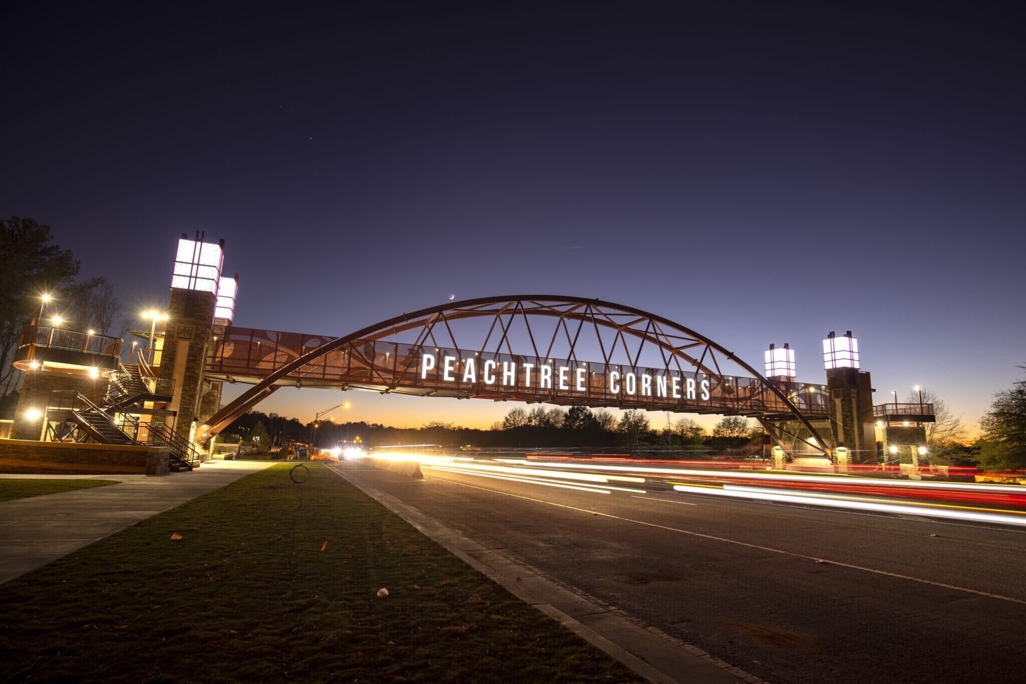 A bridge with the text "PEACHTREE CORNERS" spanning over a road at dusk.