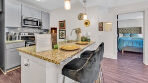 A modern kitchen with granite countertops, stainless steel appliances, and a bar area with black chairs.