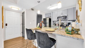 A modern kitchen with granite countertops, stainless steel appliances, and bar stools.