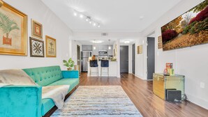 A modern living room with a teal sofa, a patterned rug, and a kitchen in the background.
