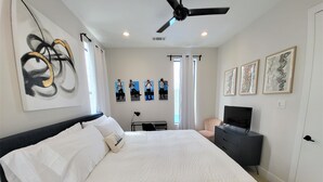 A bedroom with a bed, a ceiling fan, a TV, and artwork on the walls. - Bright Irish Channel Cottage 10 mins to FQ/Uptown (New Orleans)
