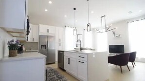A modern kitchen with white cabinets, a central island, and pendant lighting. - Bright Irish Channel Cottage 10 mins to FQ/Uptown (New Orleans)