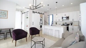 A modern apartment with a dining area, two armchairs, a sofa, a kitchen with white cabinets, and a central island. - Bright Irish Channel Cottage 10 mins to FQ/Uptown (New Orleans)