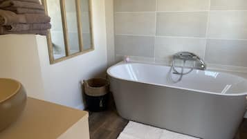 Ein modernes Badezimmer mit einer freistehenden Badewanne, einem großen Spiegel und Holzboden.