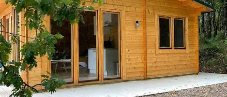 Una cabaña de madera con puerta de vidrio, rodeada de grava y árboles.