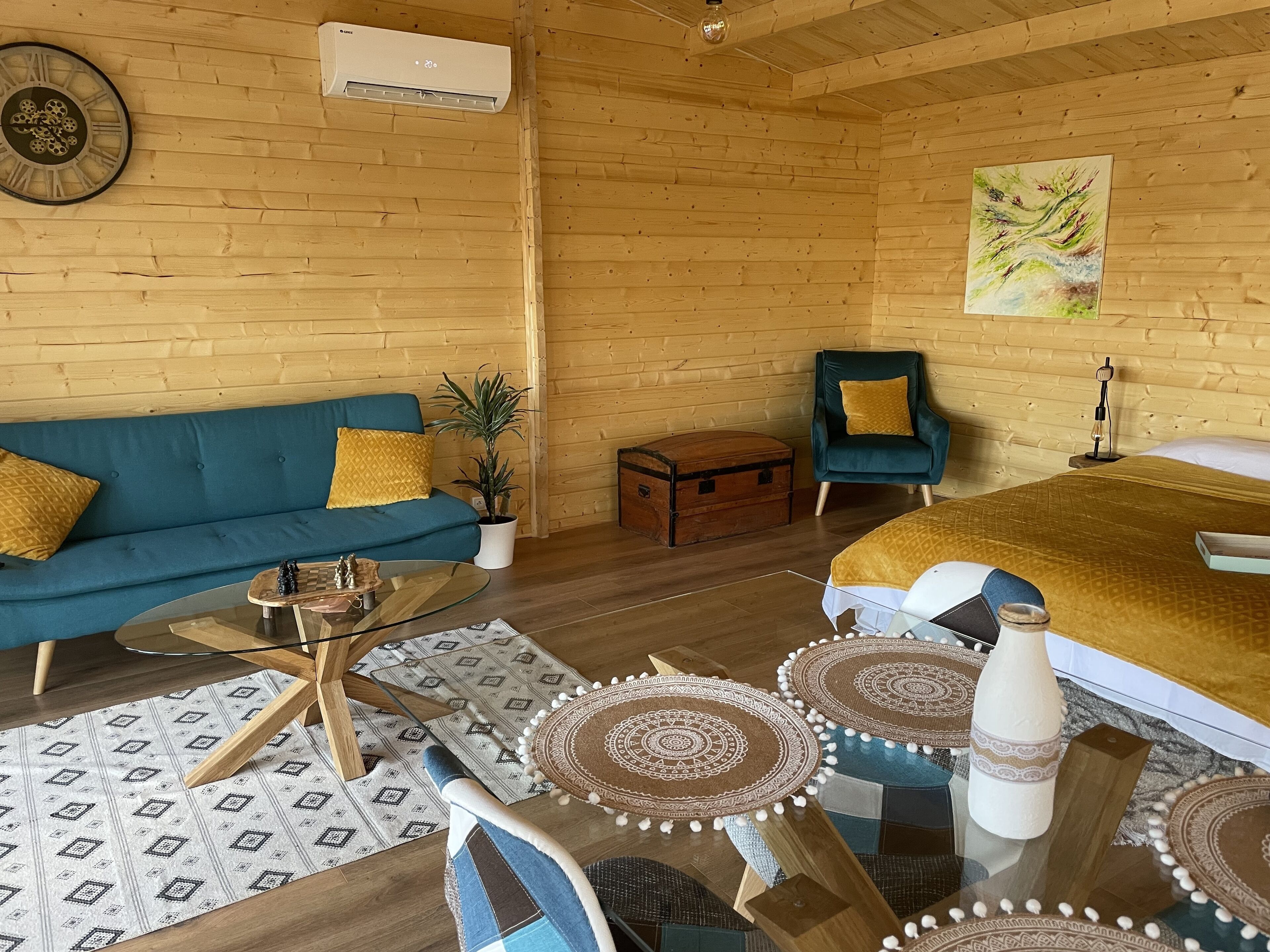 A cozy room with a blue sofa, a wooden chest, a green armchair, and a bed with a yellow blanket.