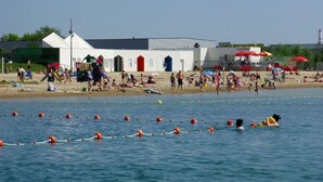 A beach with a swimming area marked by floating buoys, a white building with red doors, and beach umbrellas. - APARTMENT GÎTE DE L'OBERHARTH COLMAR ALSACE (Colmar)