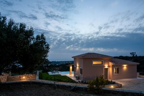 A modern house with a swimming pool, surrounded by greenery and a stone wall.