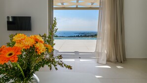 Ett rum med ett stort fönster, en platt-TV på väggen och utsikt över havet och en pool.