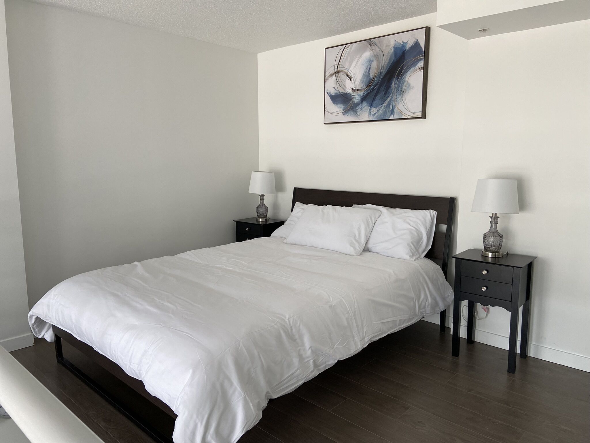 Une chambre à coucher avec un grand lit, deux tables de chevet avec des lampes et un tableau au mur.