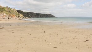 A beach with a sandy shore, a rocky cliff, and a calm sea under a cloudy sky. - The Moonbeach Cabin (St Austell)