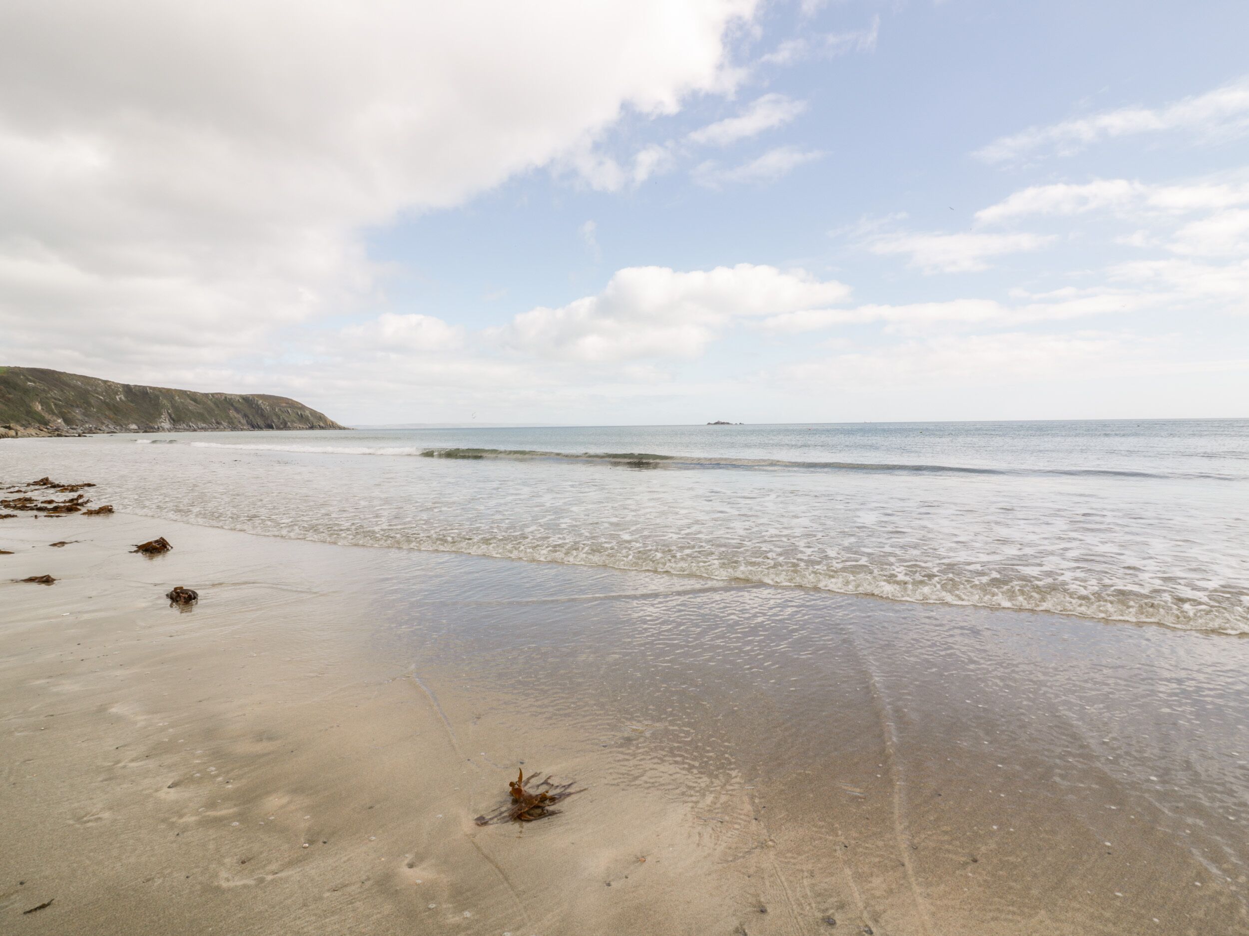 A beach with calm waves, a sandy shore, and distant cliffs.