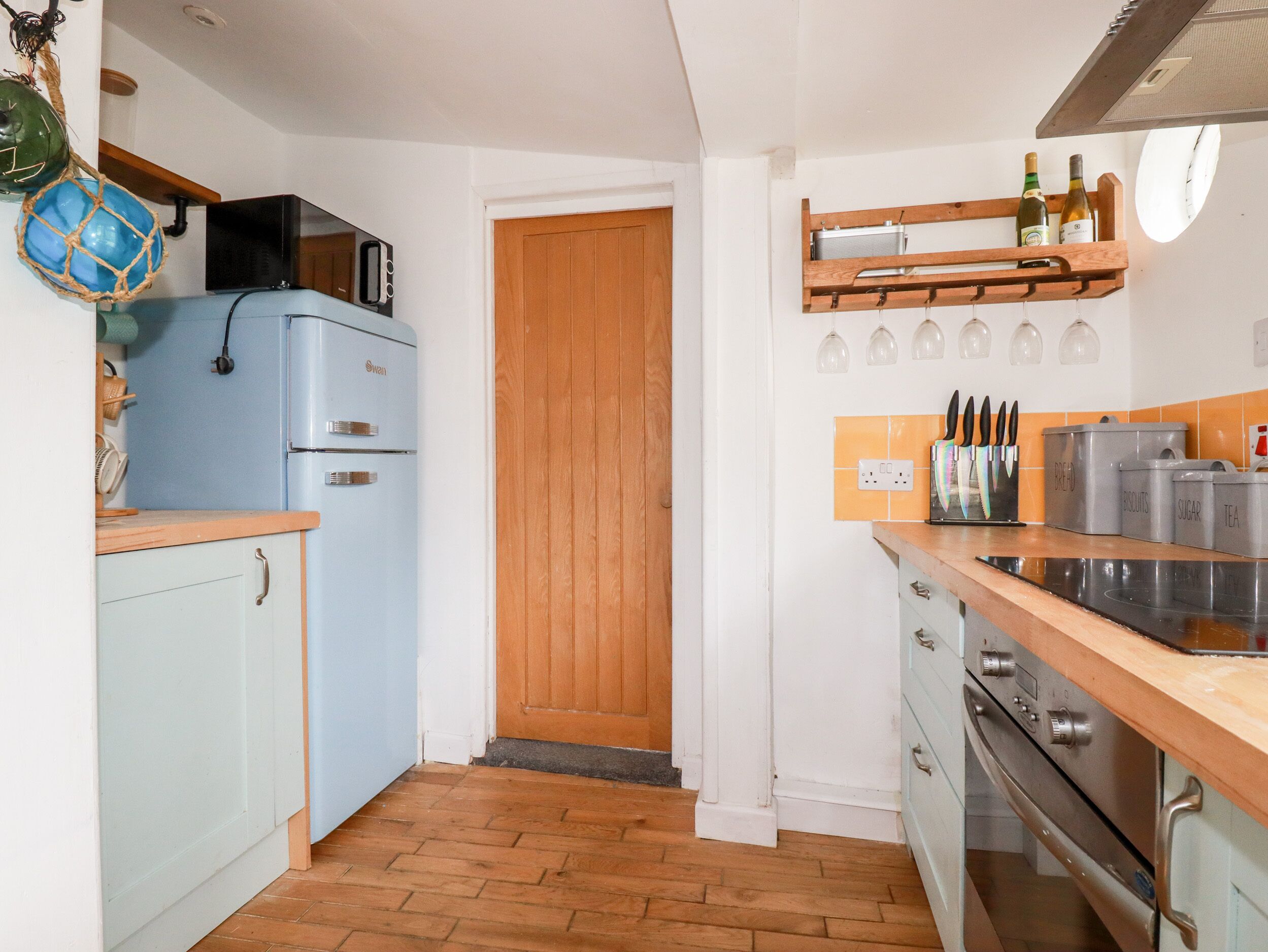 Una cucina compatta con un frigorifero in stile vintage, una porta in legno e un piano di lavoro con contenitori portaoggetti etichettati 'BREAD', 'SUGAR' e 'TEA'.