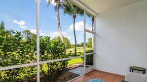 Una habitación con un ventanal grande, una mesita pequeña y un reposapiés azul con estampado.