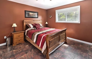 A bedroom with a wooden bed, a nightstand, a lamp, and a window with a view of trees. - Cozy Cottage Getaway - 6 Acres -3 Bedrooms! (Markdale)
