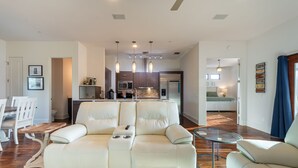 A modern living room with a white leather sofa, a glass coffee table, and a dining area with white chairs.