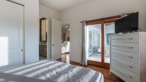 A bedroom with a bed, a dresser, a television, and a sliding glass door leading to a balcony.