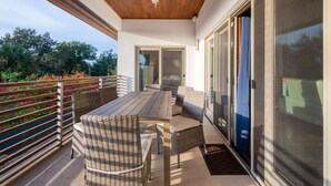A covered patio with a table and chairs, a ceiling fan, and a view of greenery.