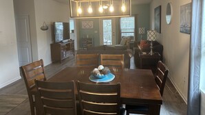 A dining area with a wooden table, chairs, and a chandelier. There is a television on a stand and a cabinet in the background. - Beautiful 3 Bedroom Condo in Barefoot Landing (North Myrtle Beach)