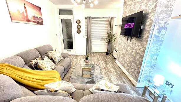 A living room with a sofa, a coffee table, a TV mounted on the wall, and a door with a mirror and decorative items. - Modern  -2 Bed Room House very Spacious  (Kingston upon Hull)