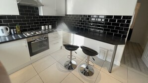 A modern kitchen with black and white tiles, stainless steel appliances, and two bar stools. - Modern  -2 Bed Room House very Spacious  (Kingston upon Hull)