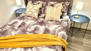 A bed with a patterned bedspread, two pillows, a yellow throw blanket, and two bedside tables with lamps. - Modern  -2 Bed Room House very Spacious  (Kingston upon Hull)