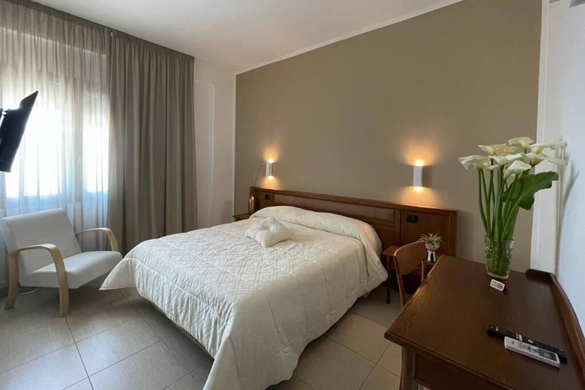 A hotel room with a bed, a chair, a desk, a TV, and a vase with flowers.