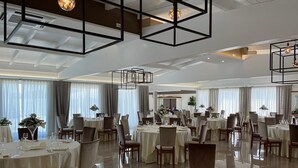 A spacious dining area with round tables, chairs, and hanging light fixtures. - Hotel Posidonia (Porto Cesareo)