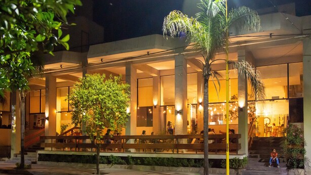 A building with a covered outdoor seating area, palm trees, and a staircase leading to an entrance. - Catalina Hotel (San Pedro de Jujuy)