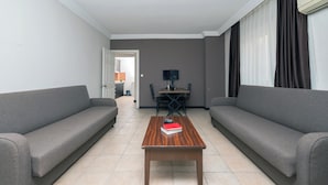 Ein modernes Wohnzimmer mit zwei grauen Sofas, einem Couchtisch mit einem Buch, einem Esstisch mit Stühlen und einem Fernseher an der Wand.