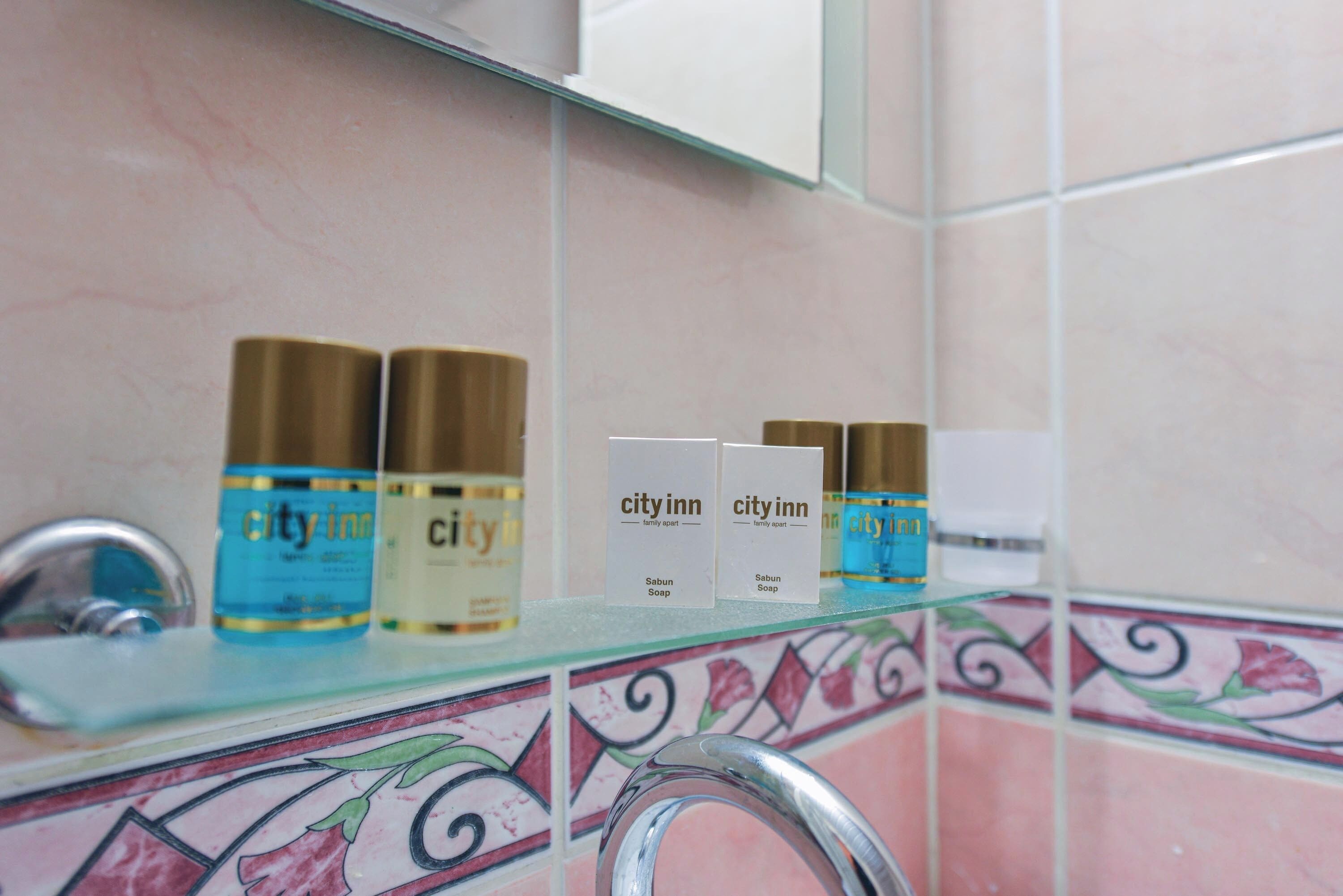 A bathroom shelf with toiletries including bottles of 'city inn' soap and shampoo.