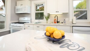 Une cuisine avec des armoires blanches, un fourneau et un saladier rempli de citrons sur le comptoir.