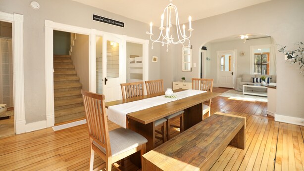 Un coin repas avec une table en bois, des chaises et un lustre. Un escalier mène à une autre pièce.