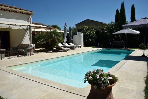 A swimming pool with lounge chairs and umbrellas, surrounded by potted plants and a patio area.