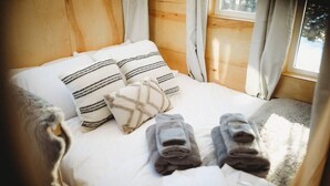 Un lit bien fait, avec des oreillers et des serviettes pliées, une fenêtre avec des rideaux et un mur en bois.