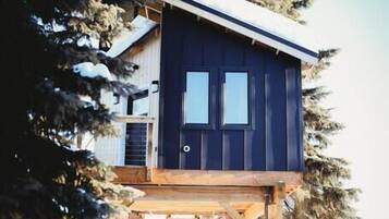 A wooden cabin on stilts surrounded by snow and trees.