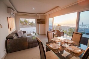 Un salon moderne avec une table à manger en verre pour quatre personnes, un canapé et un balcon offrant une vue sur la mer.