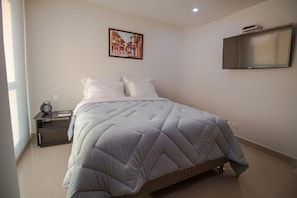 Quarto com cama, mesa de cabeceira, quadro e televisão na parede.