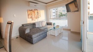 A living room with a grey sofa, a glass coffee table, and a TV mounted on the wall. - 2S3-2 APARTAMENTO EN CARTAGENA CON WIFI (Cartagena)