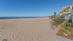 Uma praia com céu claro, areal arenoso e edifícios modernos com varandas.