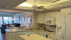 A modern kitchen with white cabinetry, a central island with stools, a microwave, a refrigerator, and a ceiling fan. - Luxurious Penthouse condo @ Pointe Santo with magnificent ocean and garden views (Sanibel)