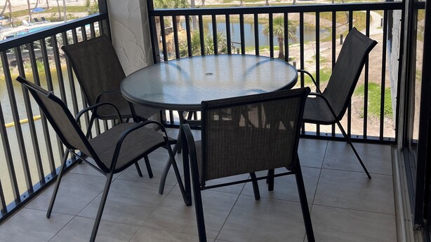 A balcony with a round table and four chairs, overlooking a beach with palm trees and the ocean. - Luxurious Penthouse condo @ Pointe Santo with magnificent ocean and garden views (Sanibel)