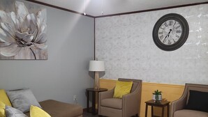 Una sala de estar con ventilador de techo, un reloj y un cuadro floral.